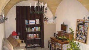A cozy living room with a sofa, a bookshelf, a dining table with chairs, a TV, and a red potted plant.