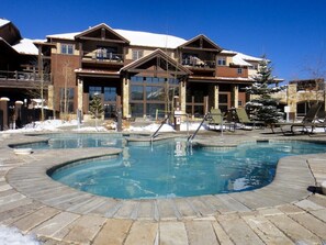A pool area with a stone deck, a building with multiple balconies, and a snow-covered roof. -  GRAND TIMBER LODGE, Breckenridge 2 bedroom, rent a full 2027 week! (Breckenridge)