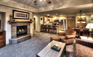 A spacious living room with a fireplace, a cozy seating area, and a kitchen in the background. -  GRAND TIMBER LODGE, Breckenridge 2 bedroom, rent a full 2027 week! (Breckenridge)