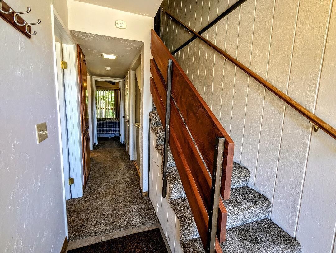 Un pasillo que conduce a una escalera con barandilla de madera y un revestimiento de pared con diseño.