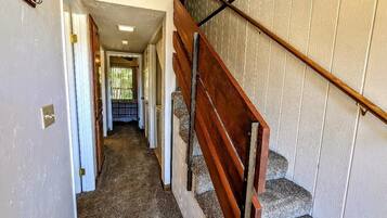 Un pasillo que conduce a una escalera con barandilla de madera y un revestimiento de pared con diseño.
