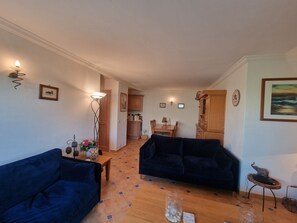 Un salon avec deux canapés sombres, une table basse en bois, un lampadaire et un coin repas comprenant une table et des chaises.