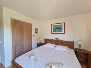 Une chambre à coucher avec un lit en bois, deux tables de chevet avec des lampes, une armoire en bois et un tableau encadré au mur.