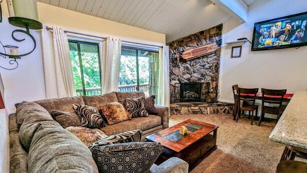 Ein gemütliches Wohnzimmer mit Kamin aus Stein, einer bequemen Couch und einem Essbereich mit Stühlen.