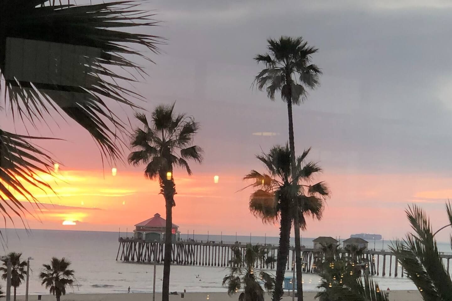 A beach scene with palm trees, a pier, and a sunset.
