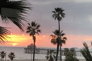 A beach scene with palm trees, a pier, and a sunset. - BEACH BUNGALOW IN THE HEART OF SURF CITY 5BR 3BA - Work place friendly (Huntington Beach)