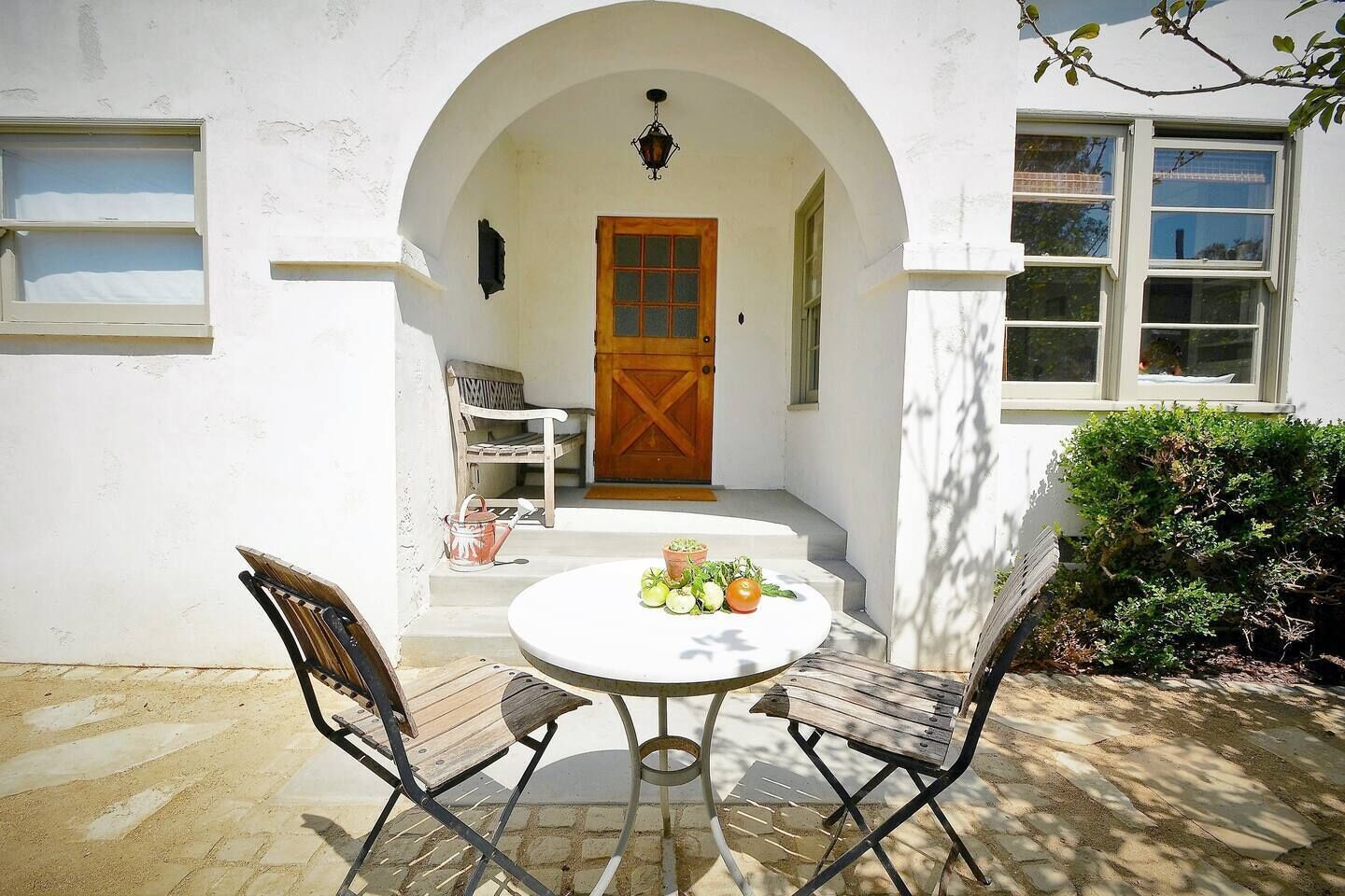 An outdoor seating area with a table and two chairs, a wooden door, and a small garden with plants.