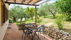Une terrasse extérieure avec une table et des chaises, un mur en pierre et une vue sur des oliviers.