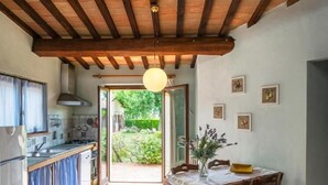 Une cuisine avec un plafond en bois, un coin repas avec une table et des chaises, et une vue sur un jardin par une porte ouverte.