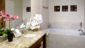 Ein Badezimmer mit Marmorwaschbecken, einem großen Spiegel, einer Badewanne und drei Wandbildern.