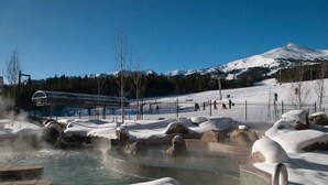 Schneebedeckte Landschaft mit einem Thermalgebiet, einer Skipiste und einem Berg im Hintergrund.