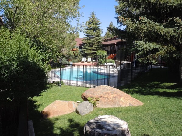 A swimming pool surrounded by a fence, with a lawn and large rocks in the foreground.