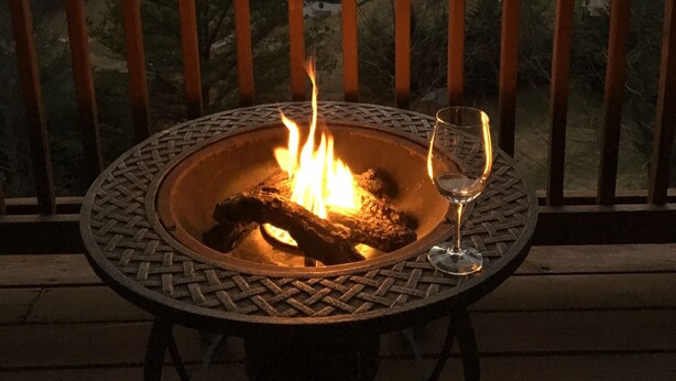 Ein Feuerkorb mit einem Weinglas auf einer Holzdielen-Terrasse mit Bergblick.