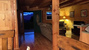 Ein gemütliches Blockhaus-Interieur mit Holzwänden, einer Couch, einem Essbereich und Bergblick durch eine Tür.
