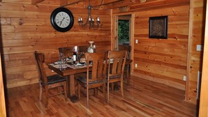 Ein Esszimmer mit Holzwänden, einem Holztisch, Stühlen, einer Uhr und einem Kronleuchter.