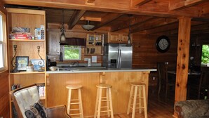 Ein Holzhütten-Interieur mit Küchenbereich, Holzbarhocker, einem Esstisch und einer Uhr an der Wand.
