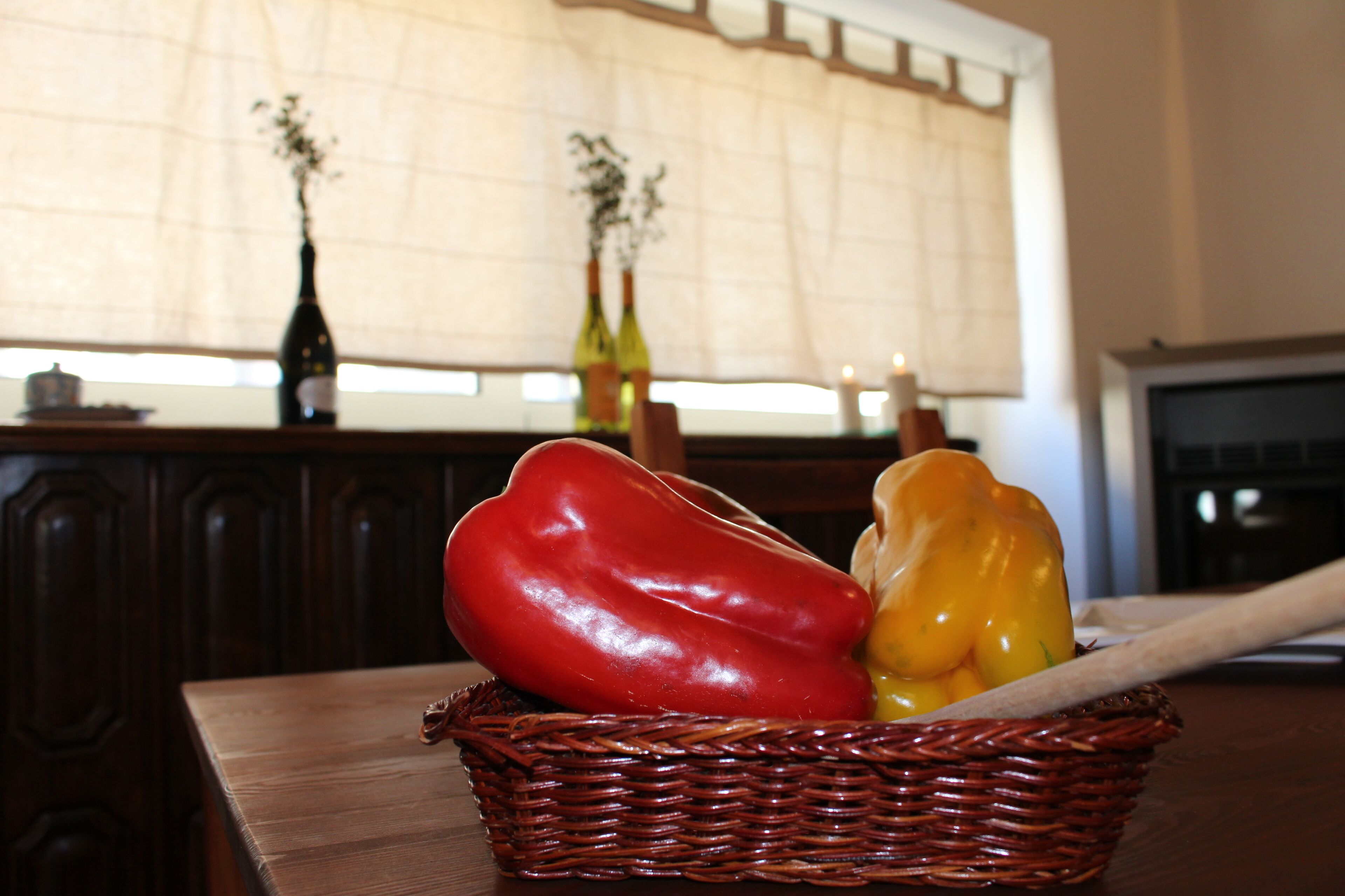 A wicker basket with red and yellow bell peppers on a wooden table.