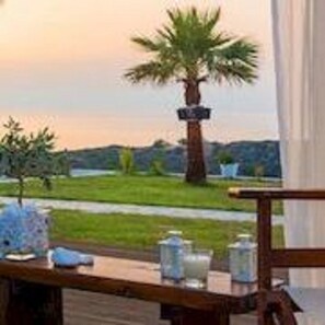 A wooden deck with a table set for dining, overlooking a grassy area with a palm tree and a signpost.