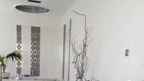 A modern bedroom with a large bed, a vase with branches, and a bathroom in the background. - Luxury White  Suite(2 Persons) (CHANIA)