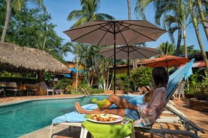 A poolside area with lounge chairs, umbrellas, and a dining table with a plate of food and a drink. - Authentic pool-side apt studio w/ full kitchen, 1min walk to beach, free yoga (Puerto Escondido)