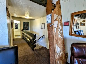 Un pasillo con una escalera de madera, un banco y un espejo en la pared.