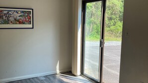 A room with a large sliding glass door leading to an outdoor area, a framed picture on the wall, and a wooden floor.