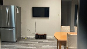 A compact kitchen with a built-in refrigerator, a flat-screen TV mounted on the wall, and a dining area with a wooden table and chairs.