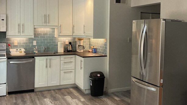 A modern kitchen with light-colored cabinets, a stainless steel refrigerator, and a dishwasher.