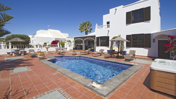A swimming pool area with lounge chairs and a hot tub, surrounded by white buildings with balconies and windows.