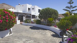 A white building with a curved driveway, surrounded by various plants and flowers.