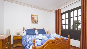 A bedroom with a wooden bed, a nightstand, a desk, a window with curtains, and a painting on the wall.