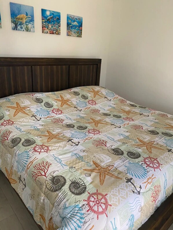 A bed with a nautical-themed bedspread featuring starfish, anchors, and ship wheels.