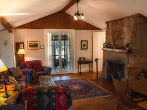 A cozy living room with a fireplace, wooden ceiling, and a large window.