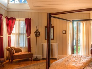 A bedroom with a four-poster bed, a wooden floor, a radiator, and a chair.