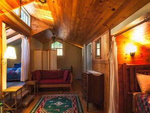 Un interior de cabaña acogedor, con techo de madera, un sofá, un aparador y una ventana.