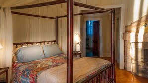 Uma cama de dossel com edredom estampado, cabeceira de madeira e uma mesa de cabeceira com abajur.