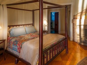 A four-poster bed with a floral bedspread, wooden headboard, and a nightstand with a lamp. - Mrs Coolidge's Cabin (Paul Smiths)