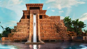 Una gran estructura de piedra con una fuente central, rodeada de palmeras y un cielo despejado.