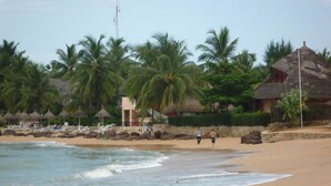 A beach with palm trees, a thatched-roof building, and a stone wall. - Dreamlike villa with infinity Jacuzzi and lagoon swimming pool (Unknown)