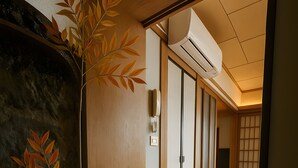 Ein traditionelles japanisches Interieur mit Tatami-Bodenbelag, einem Blumentopf, Schiebetüren und einer Decken-Klimaanlage.