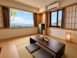 A room with tatami flooring, a wooden table with cushions, a vase with flowers, and a view of the sea. - Twilight House (New Taipei City)