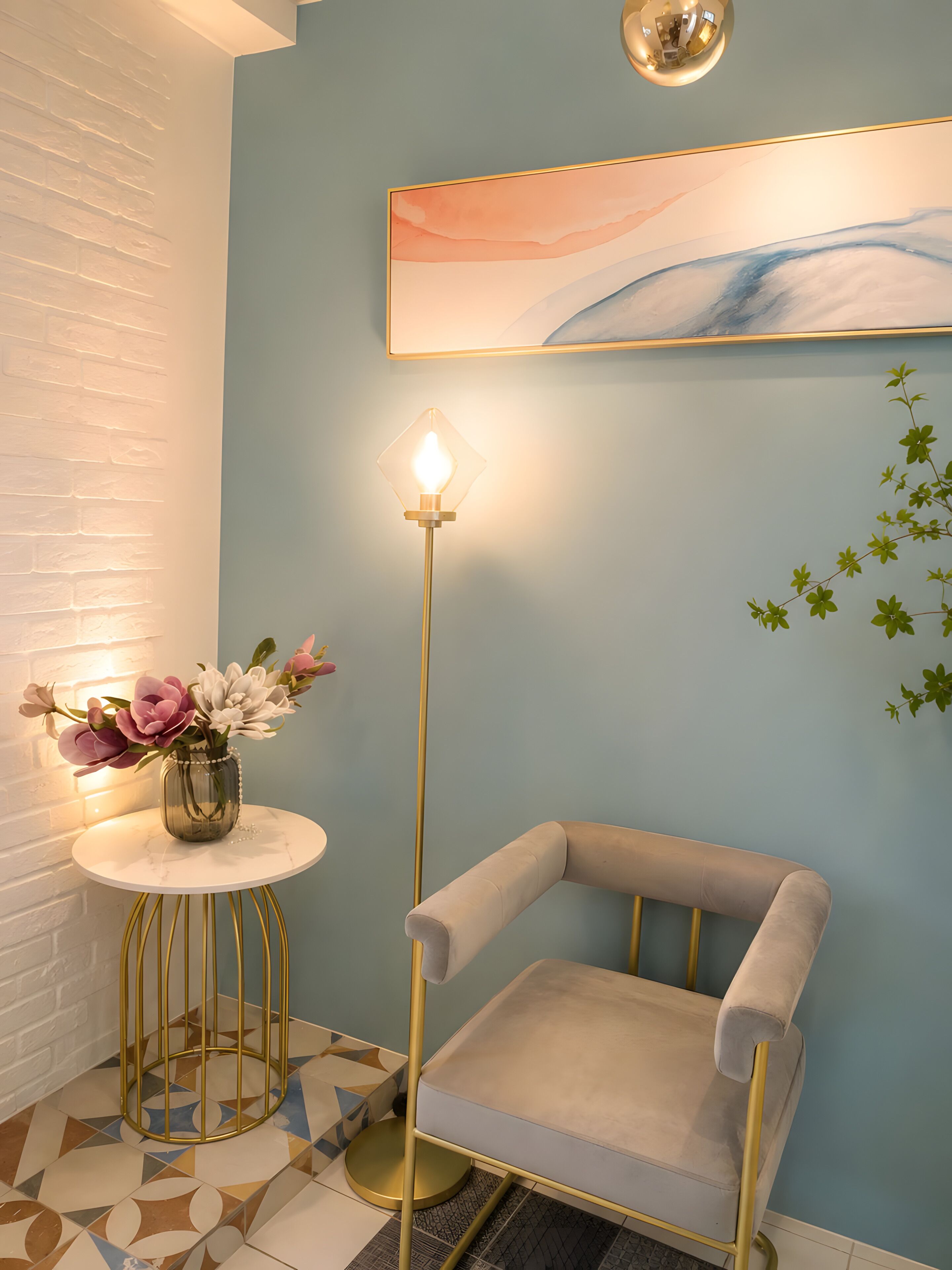 A room with a blue wall, a round table with a vase of flowers, a tall floor lamp, and a cushioned chair.