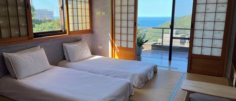 A room with two beds, a tatami mat floor, a sliding door with a view, and a hanging light fixture.
