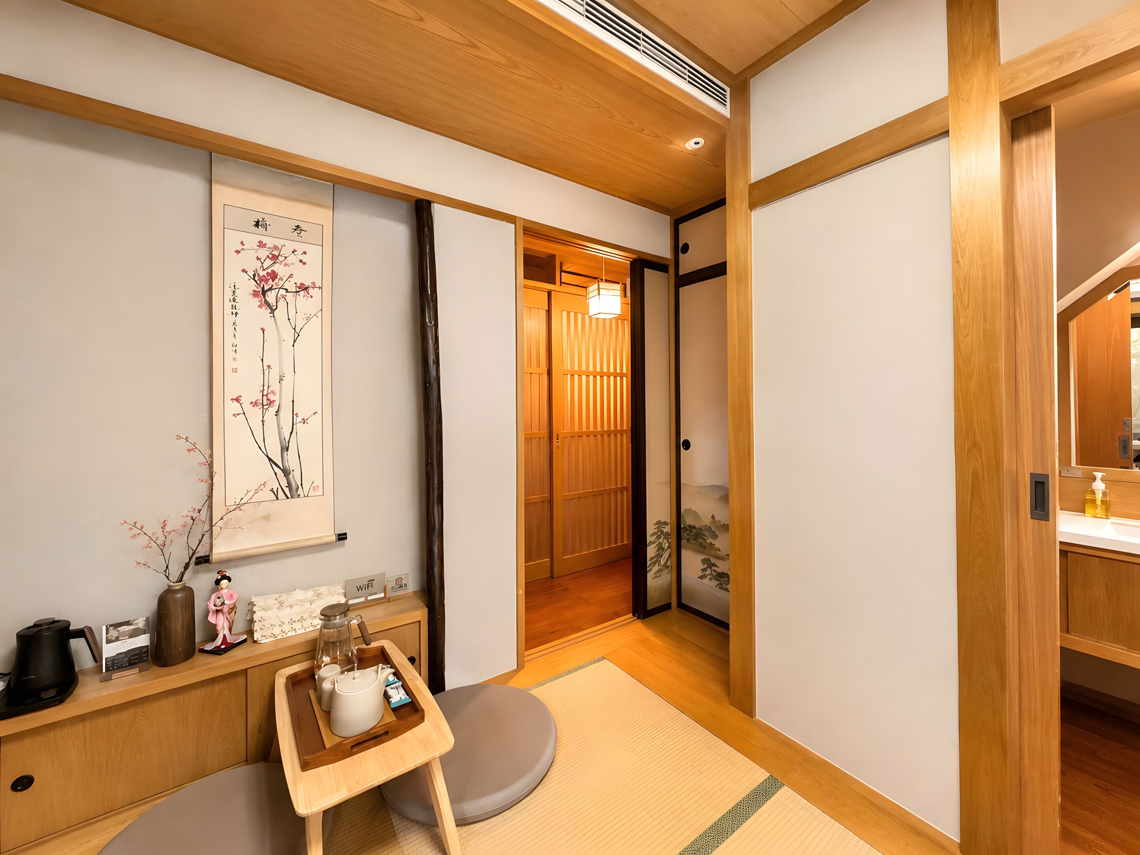 Une pièce de style japonais traditionnel, avec un sol recouvert de tatamis, une porte coulissante en papier de riz (shoji), un service à thé disposé sur un plateau et une œuvre d’art encadrée accrochée au mur.
