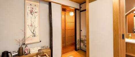 Une pièce de style japonais traditionnel, avec un sol recouvert de tatamis, une porte coulissante en papier de riz (shoji), un service à thé disposé sur un plateau et une œuvre d’art encadrée accrochée au mur.