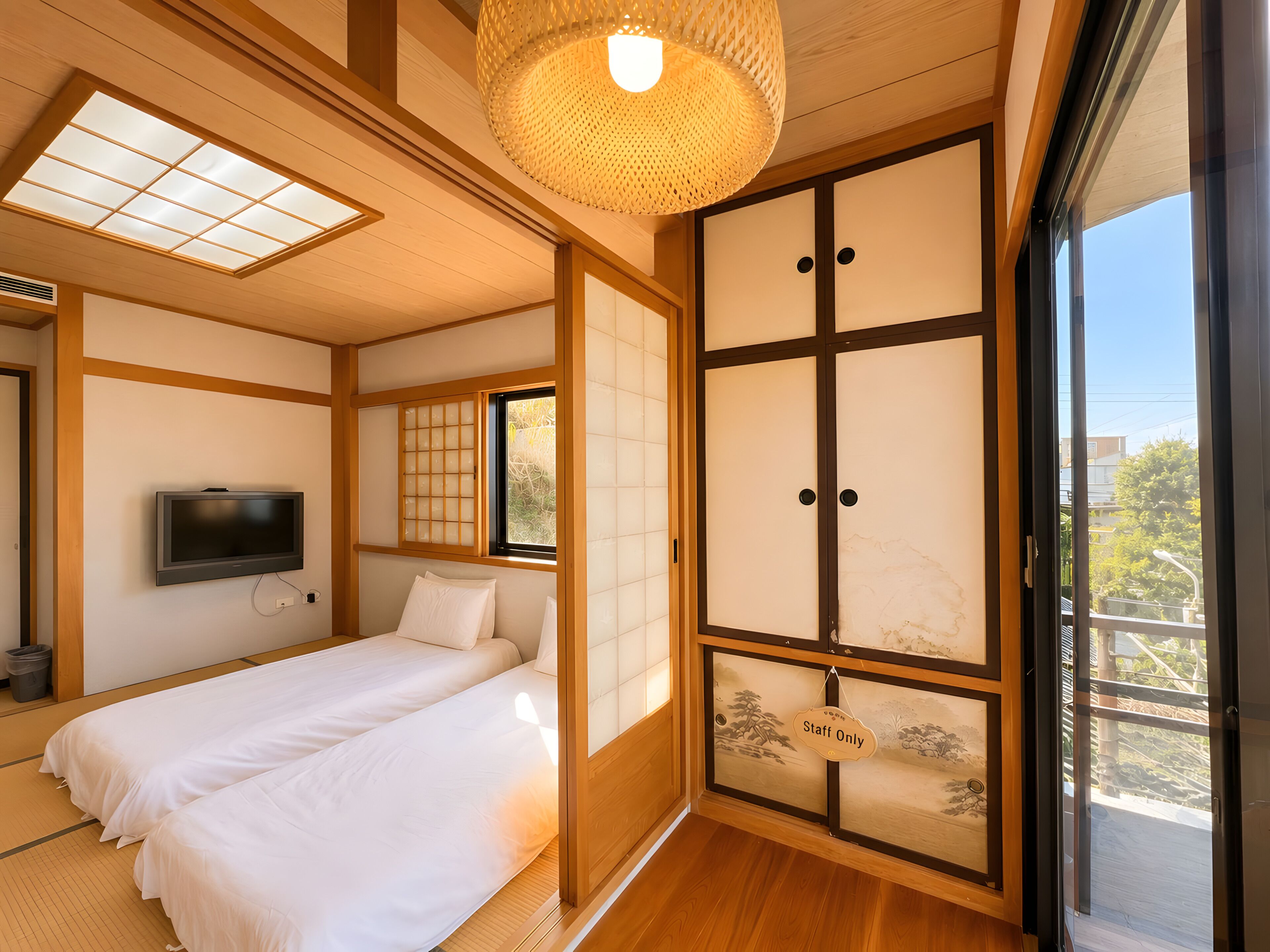 A traditional Japanese-style room with tatami flooring, a bed, a television, sliding doors, and a view of the outside.