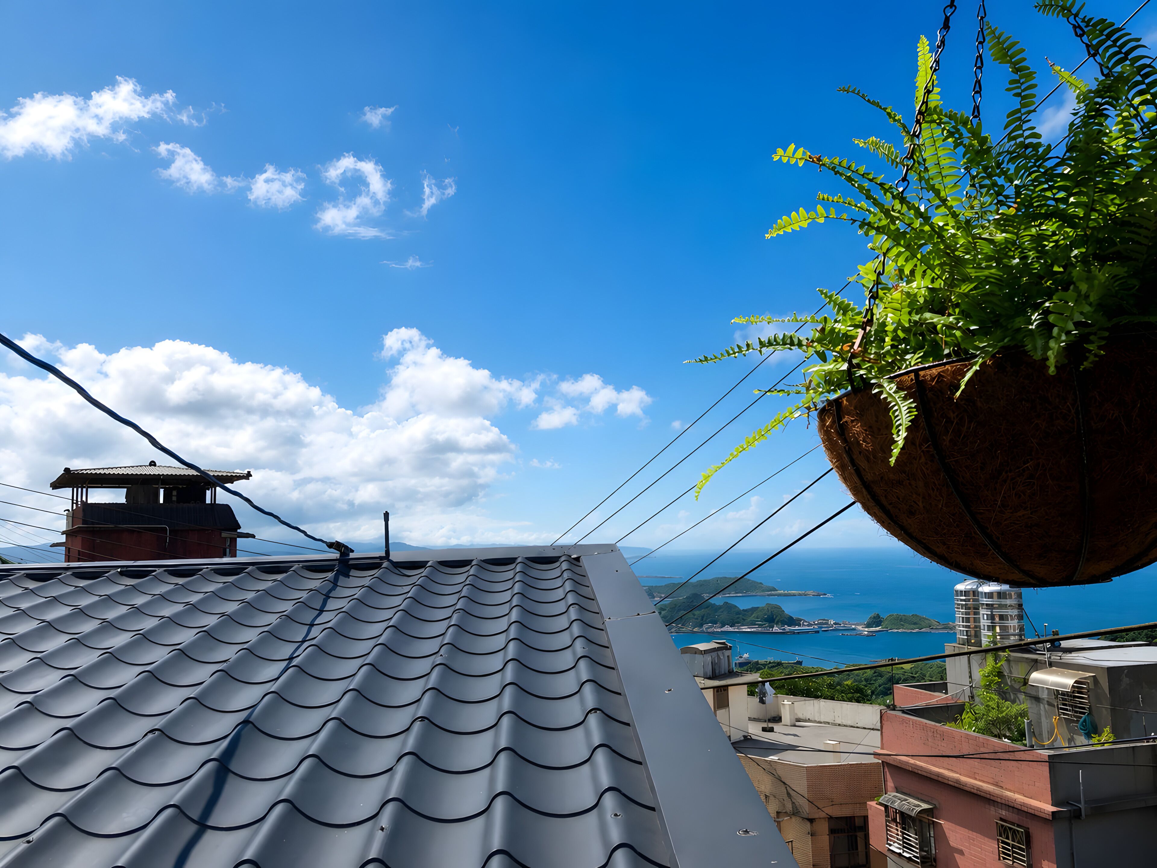 A rooftop with a tiled roof, a hanging plant, and a view of the sea.