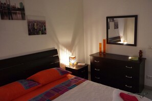 A bedroom with a bed, nightstand, dresser, and a mirror.