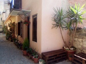 A narrow alley with potted plants lining one side and a wooden bench on the other.