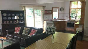 Een woonkamer met een bruine leren bank, een eettafel met een gele tafelkleed en een vaas witte bloemen.
